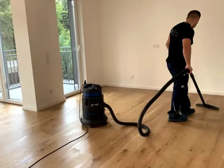 Mitarbeiter saugt Baustaub von einem neuen Holzboden in einer leeren Wohnung